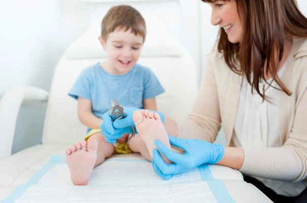 A podiatrist wearing blue gloves gently examining a young child's foot during a pediatric podiatry appointment. The child sits on an exam chair, smiling and engaging comfortably with the specialist.